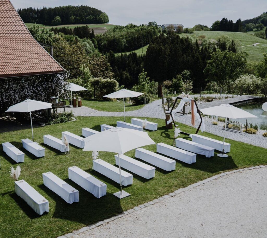 Hochzeitszeremonie im Freien mit weißen Bänken und Sonnenschirmen Bierbankhussen Garnituren mieten