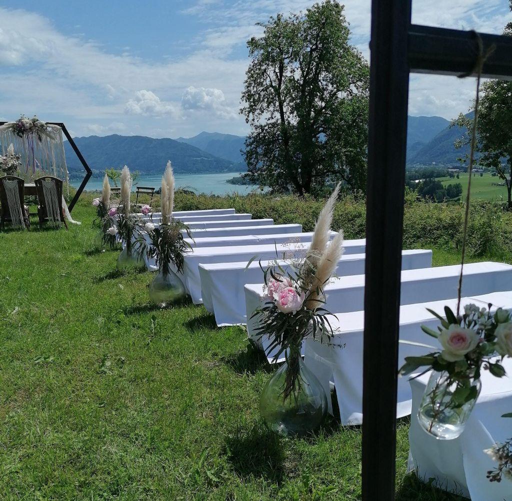 Freie Trauung im Boho-Stil am Mondsee mit weißen Bierbank Hussen und Blumendekoration in Glasvasen beim Leidingerhof.