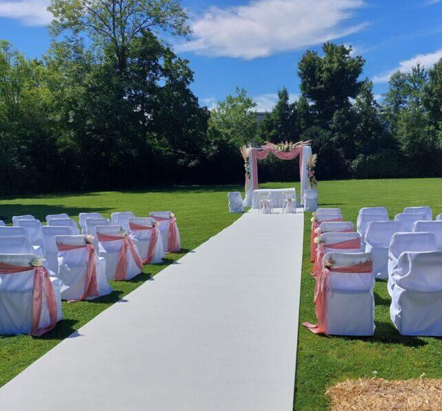 Elegante freie Trauung im Garten in Salzburg mit weißen Klappstuhlhussen und rosa Schleifen – Hochzeitsdekoration zum Mieten in Österreich.